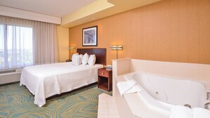 A hotel room with a large bed, a separate bathroom with a bathtub, and a window with curtains.