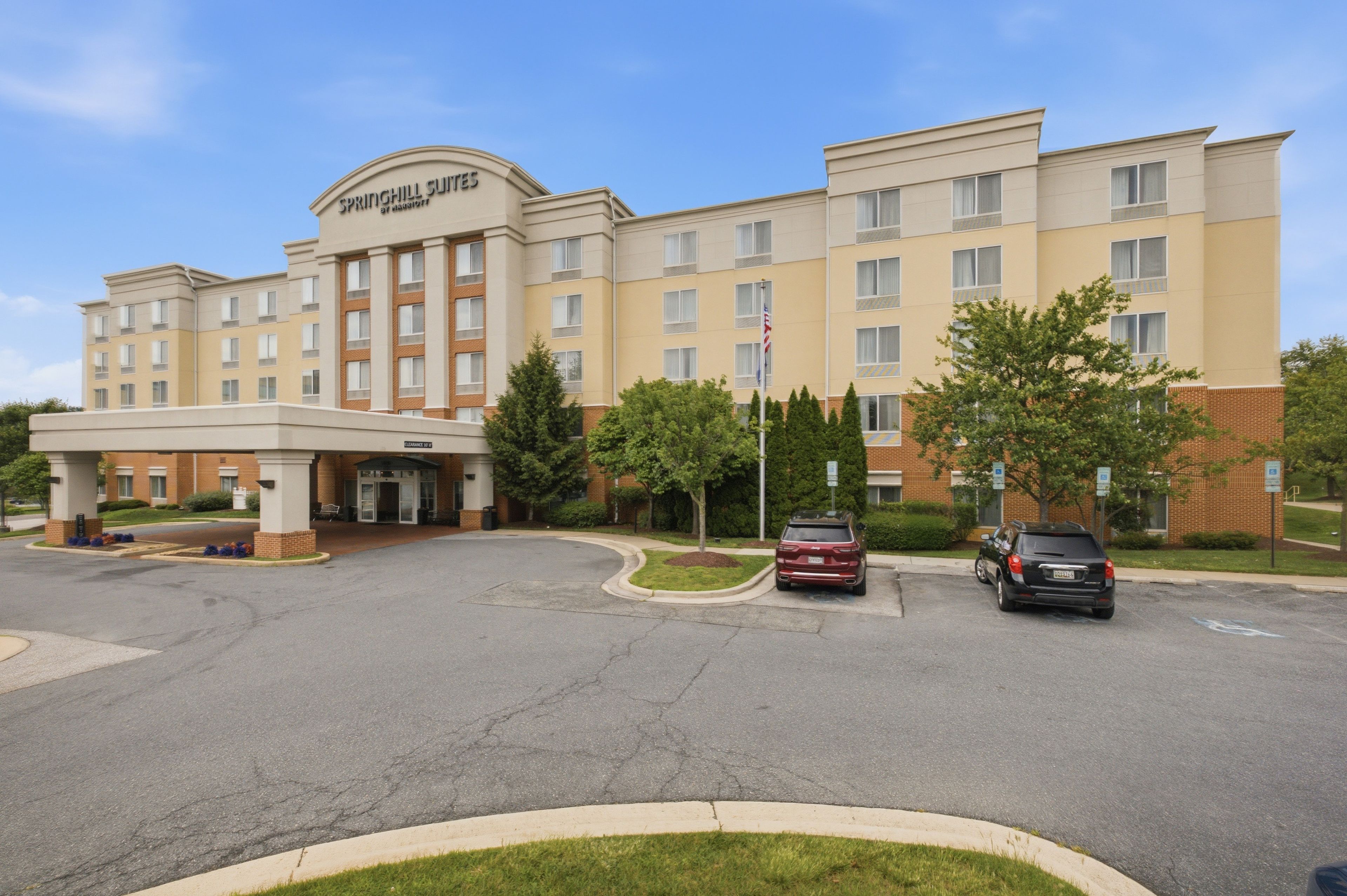 A multi-story hotel with a central entrance, parking area, and a flagpole.