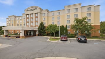 A multi-story hotel with a central entrance, parking area, and a flagpole.