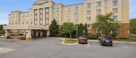 A multi-story hotel with a central entrance, parking area, and a flagpole.
