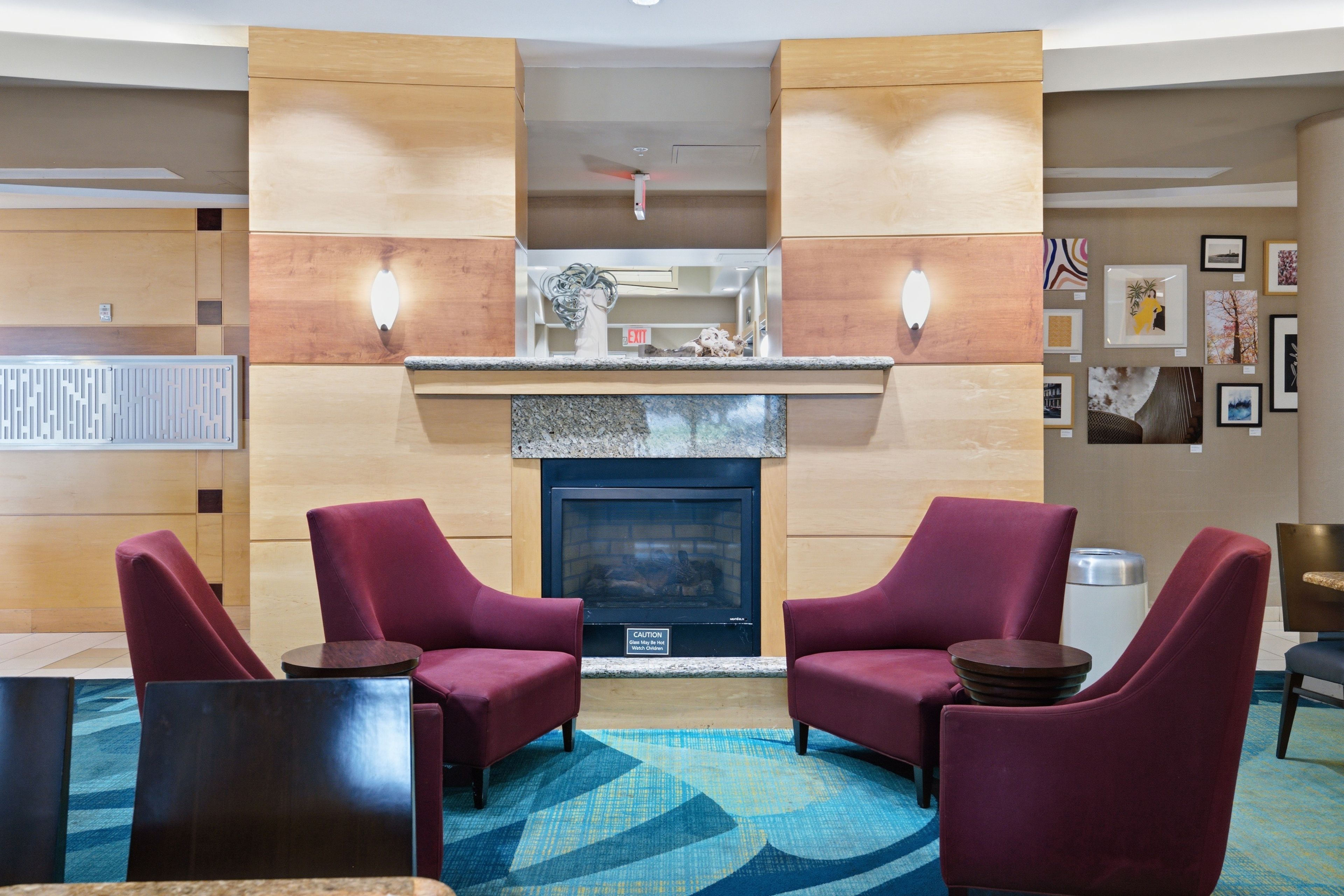 A lobby with a fireplace, two armchairs, a coffee table, and a patterned rug.