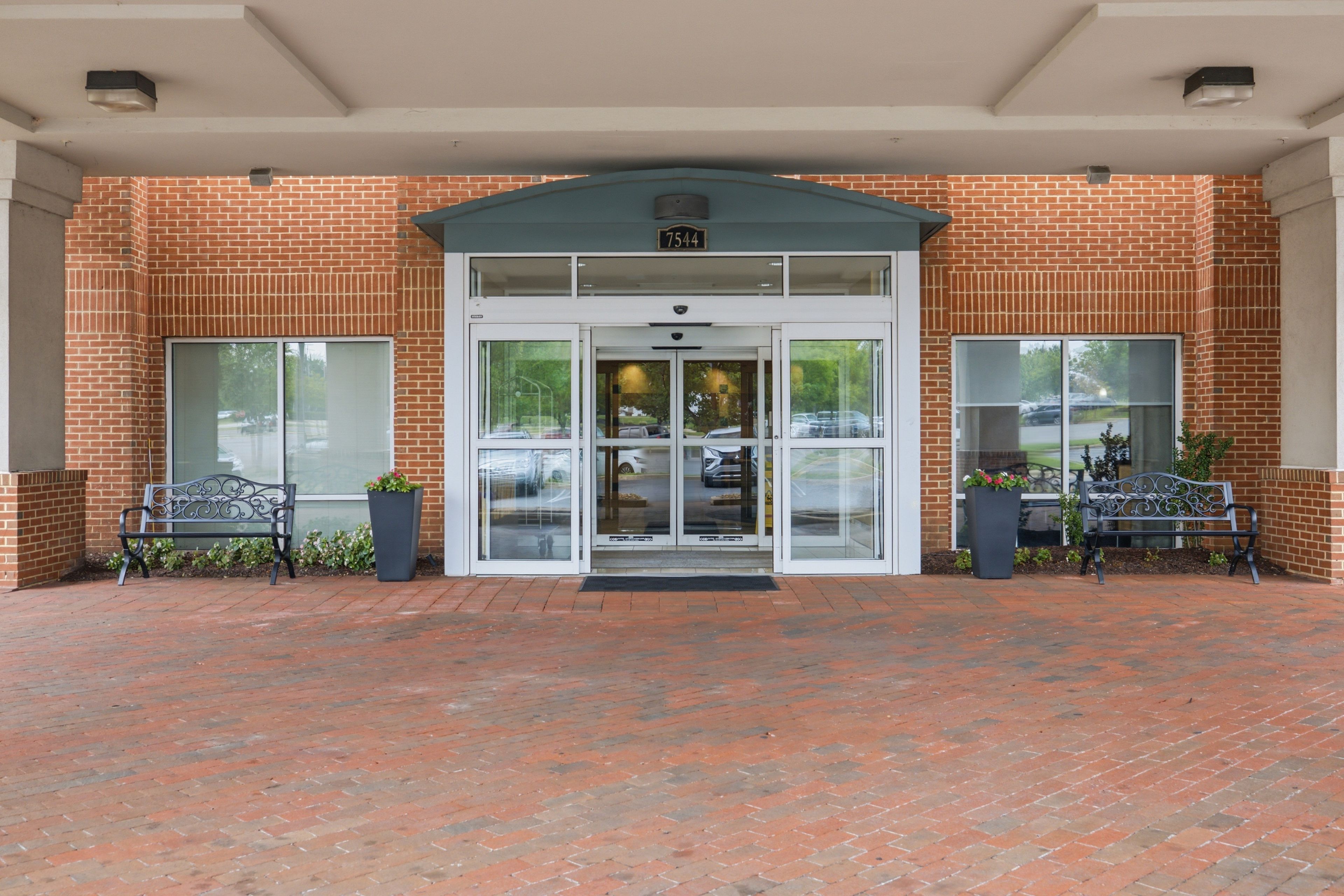 A brick building with a glass entrance, two benches, and a parking lot.