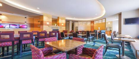 A hotel lobby with multiple seating areas, a reception desk, and a flat-screen TV mounted on the wall.