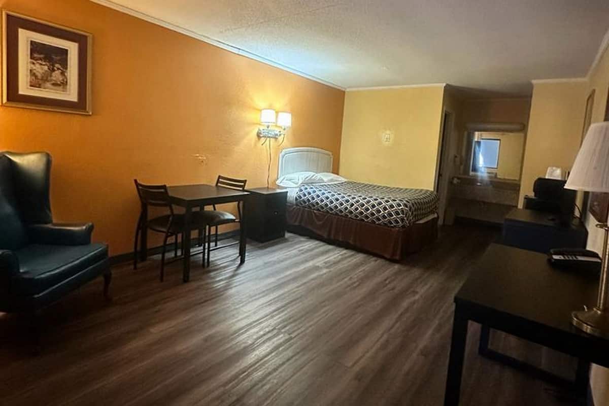 Une chambre d’hôtel de taille réduite, comprenant un lit, un bureau, une chaise, une table et une lampe.