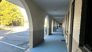 A covered walkway with arches, a parking lot, and a building with windows and vents. - Loyalty Inn Rockingham (Rockingham)
