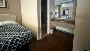A hotel room with a bed, a bathroom with a sink and mirror, and a door leading to another room. - Loyalty Inn Rockingham (Rockingham)