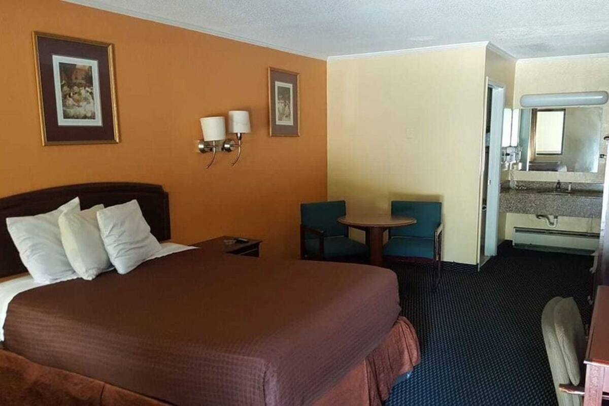 Une chambre d’hôtel avec un lit, deux chaises, une petite table, un bureau et un miroir.
