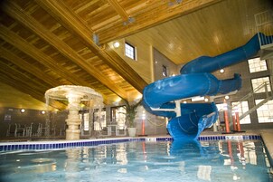Piscina interna com escorregador azul, teto de madeira e chão de azulejo.