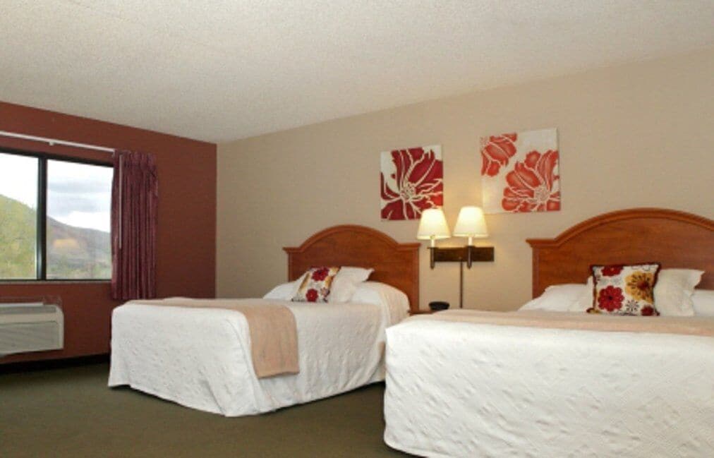 A hotel room with two beds, a window with curtains, and wall art.