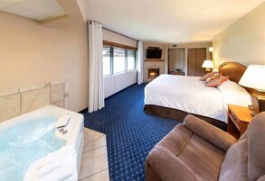 Quarto de hotel com uma cama grande, um sofá separado, lareira, televisão e banheira.