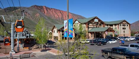 A hotel with a mountain backdrop, a parking lot, and a ski lift.