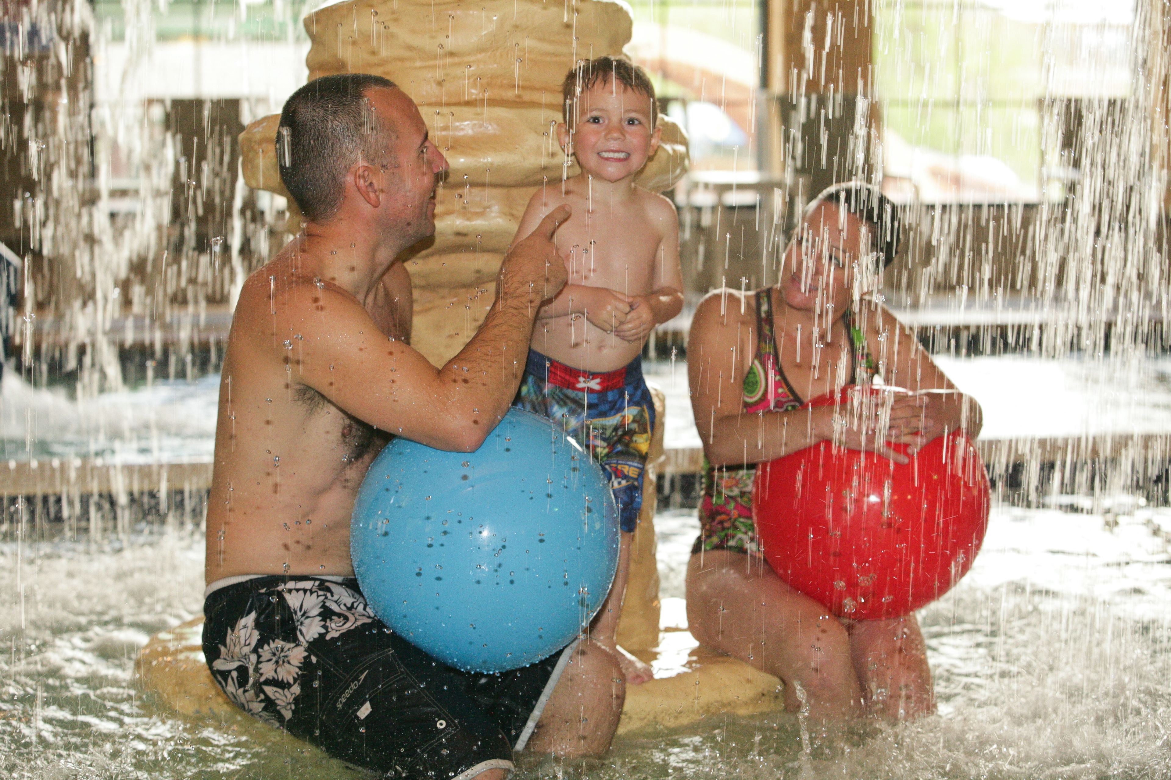 A man and a child in a water play area with a large water feature.