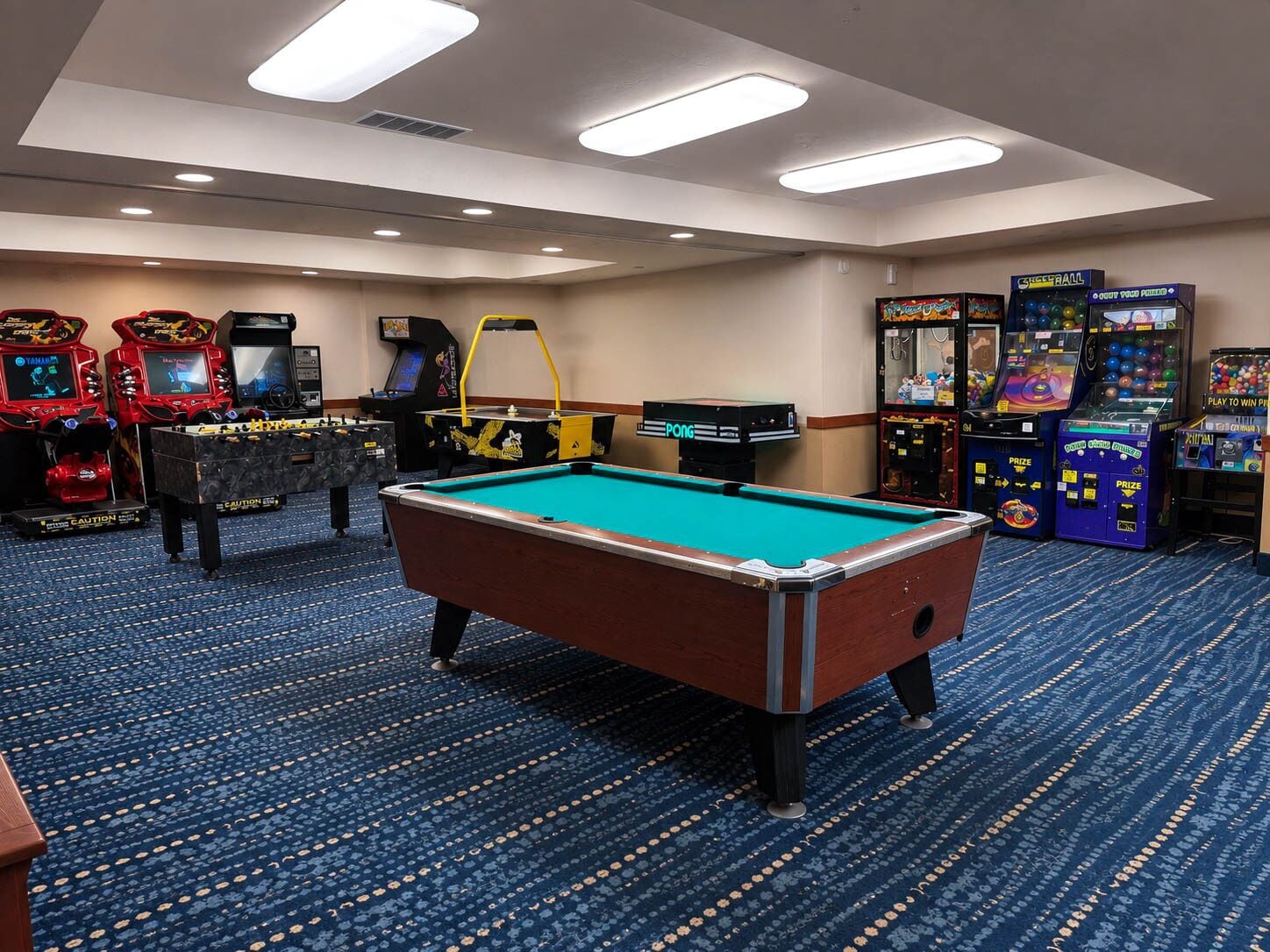 A pool table in a room with arcade games and a foosball table.