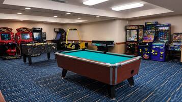 Una mesa de billar en una sala con juegos de arcade y una mesa de futbolín.