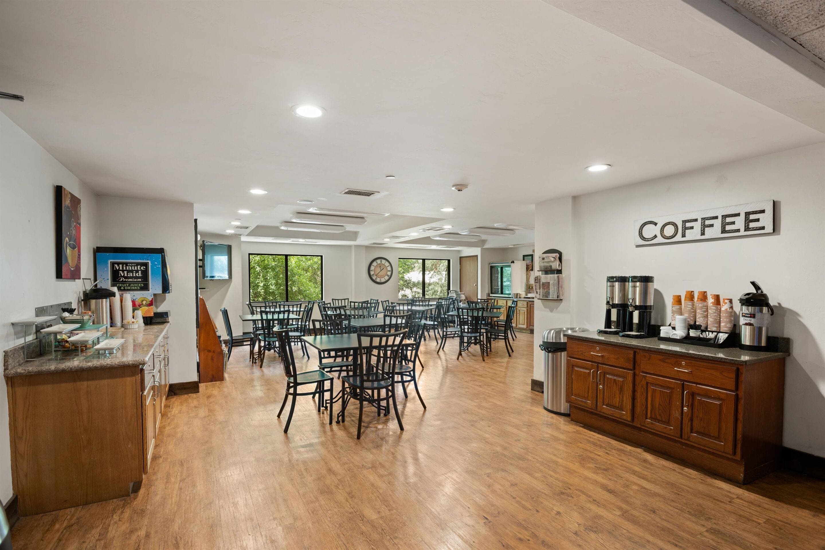 A spacious dining area with multiple tables and chairs, a coffee station, and a clock on the wall.