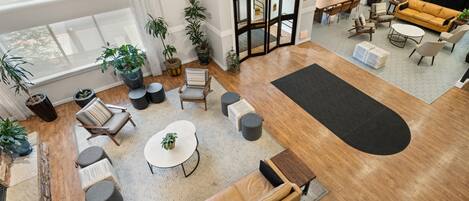 Amplia sala de estar con un sofá grande, una mesa de centro redonda y varias sillas. Se observan varias plantas en macetas, una mesa de comedor con sillas y una zona de cocina visible a través de un acceso abierto.