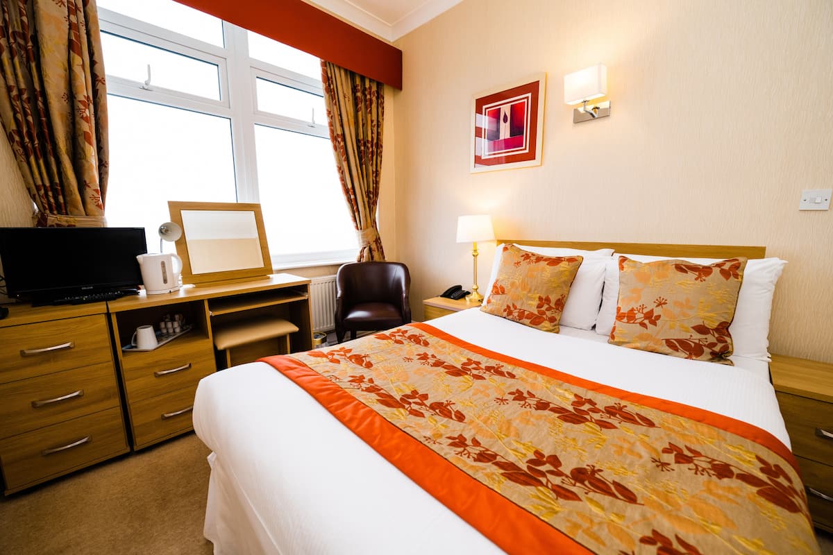 A hotel room with a bed, desk, chair, and a television.