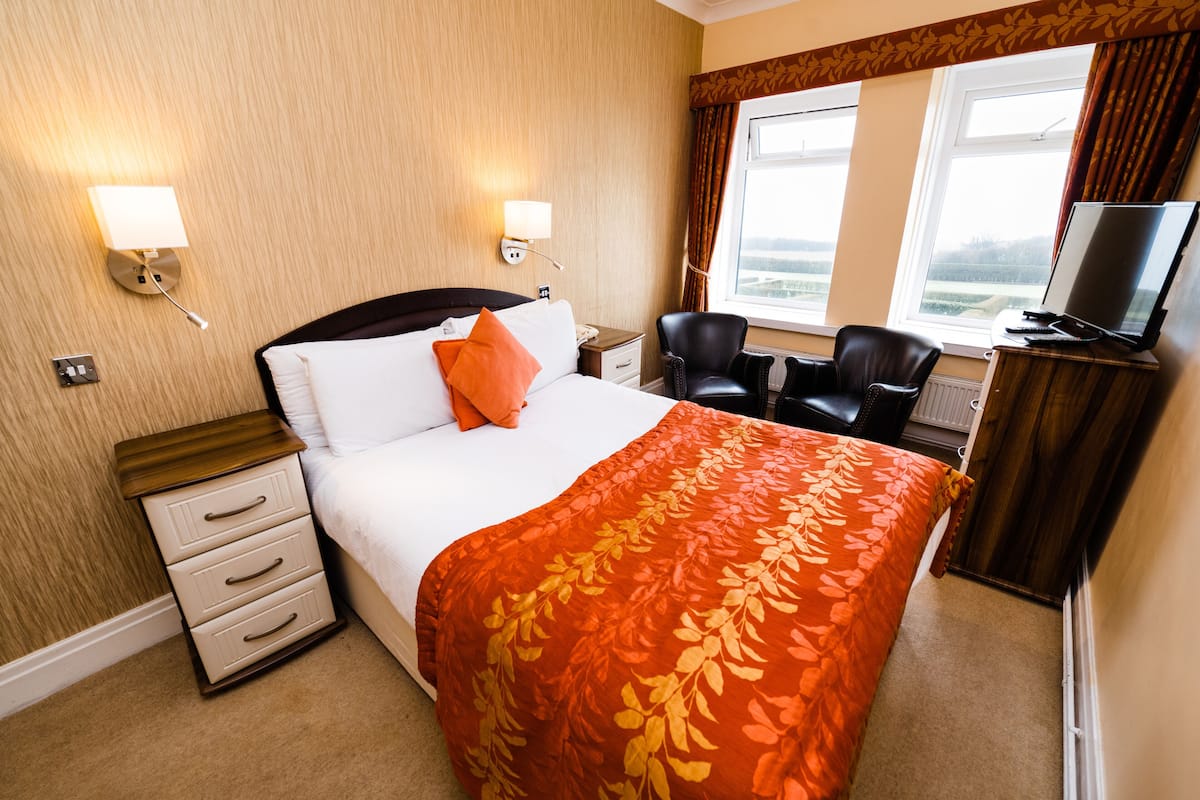 A hotel room with a bed, a desk with a computer, a chair, and a television.