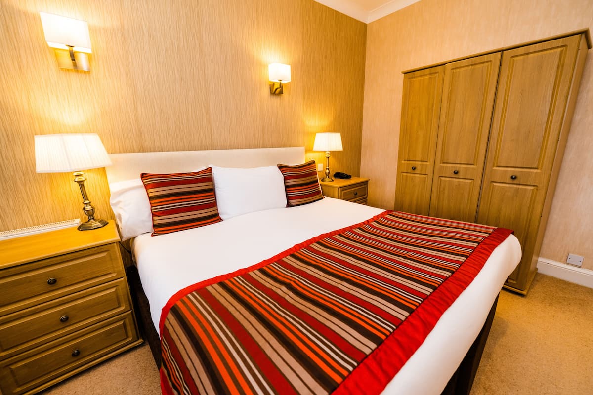 A hotel room with a large bed, two bedside tables with lamps, a wardrobe, and a wall-mounted light fixture.
