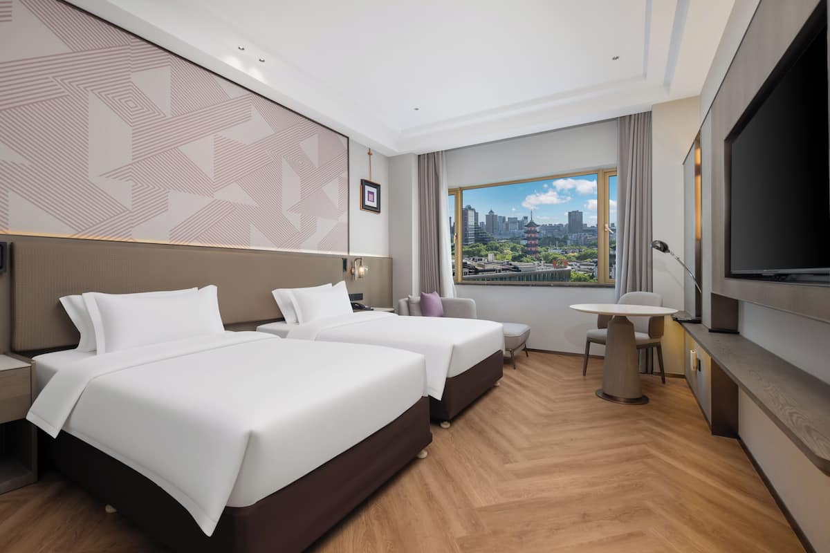 Habitación de hotel moderna con dos camas, zona de comedor y ventana grande con vistas a la ciudad.