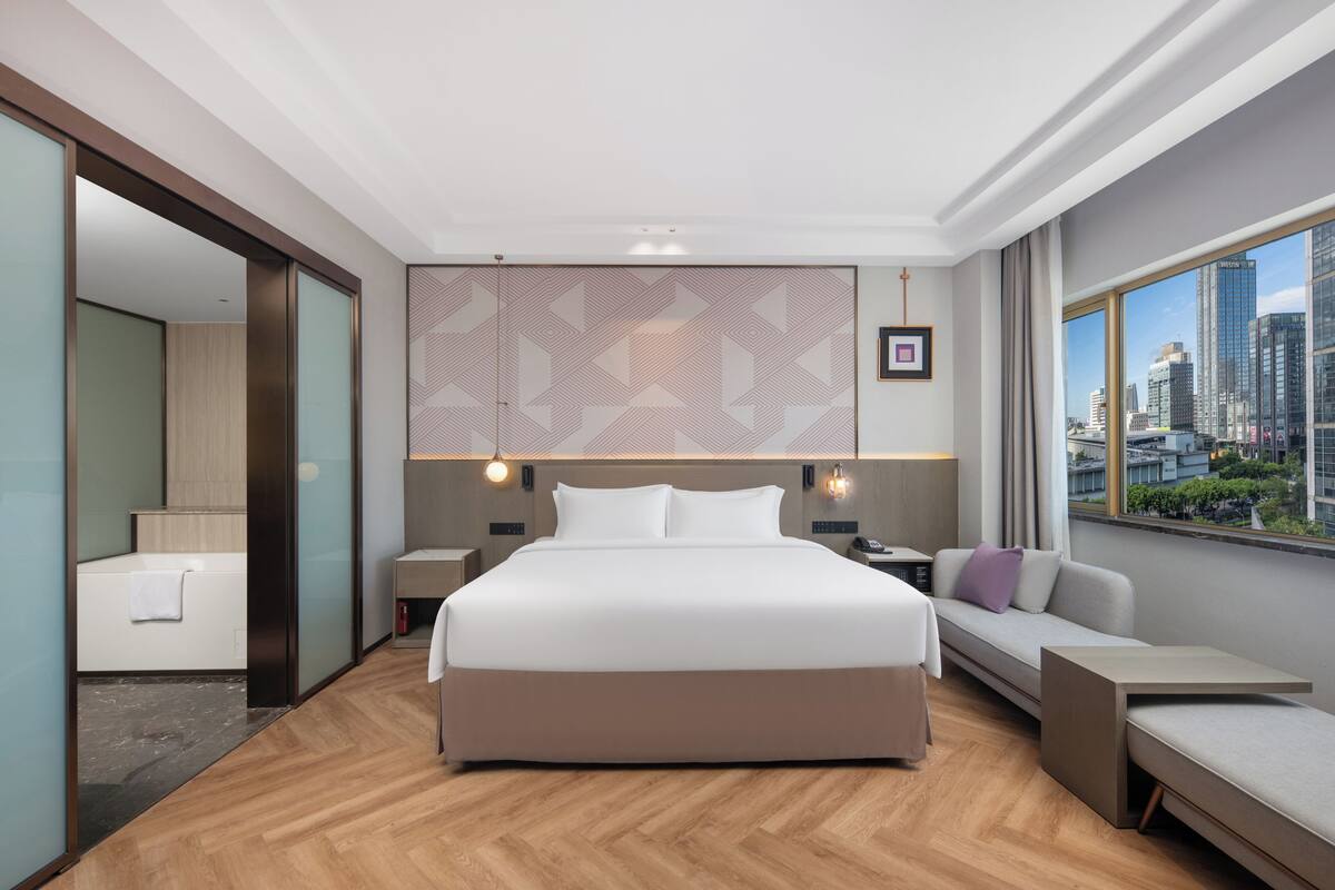 Habitación de hotel moderna con una cama grande, un sofá, un escritorio y vistas a la ciudad.