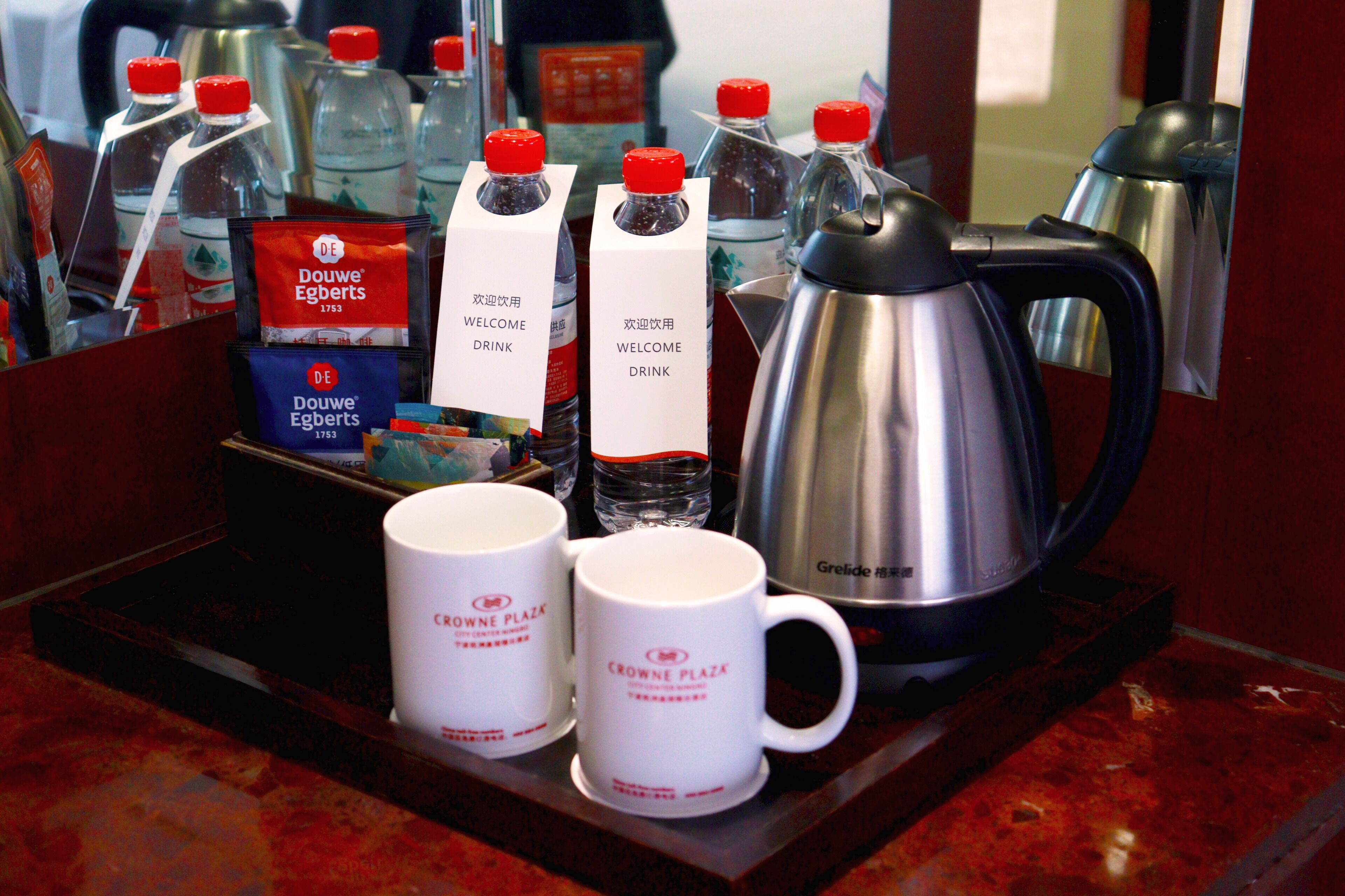 Una bandeja con dos tazas blancas, una cafetera de plata y varias botellas de agua y café.