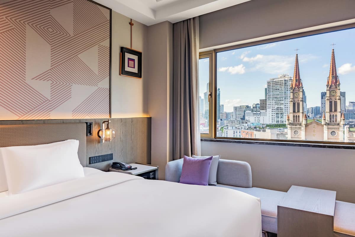 Habitación de hotel con una cama grande, un escritorio y vistas a la ciudad, incluyendo una torre de iglesia.