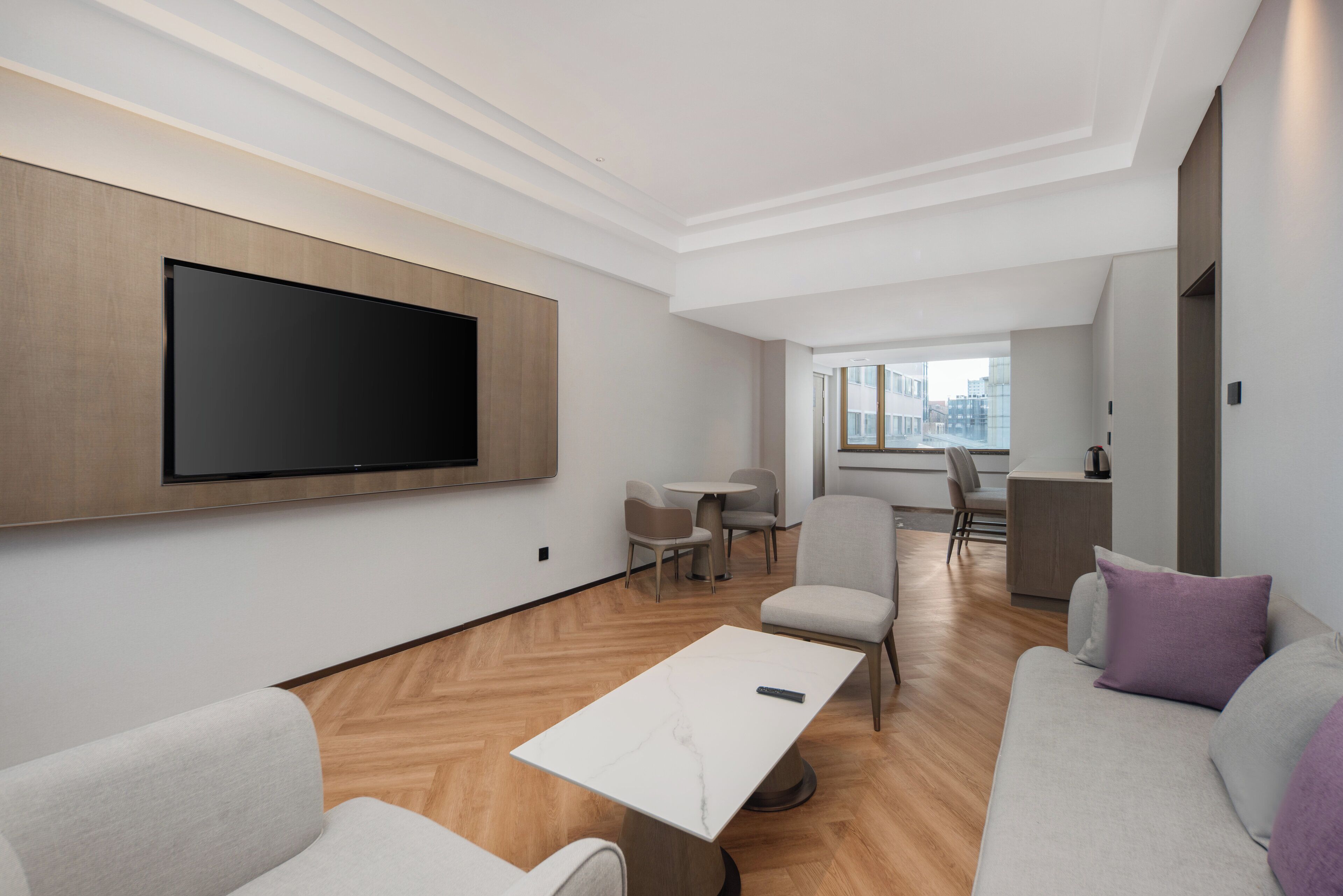 A modern living room with a flat-screen TV, a coffee table, sofas, and a dining area with chairs and a table.