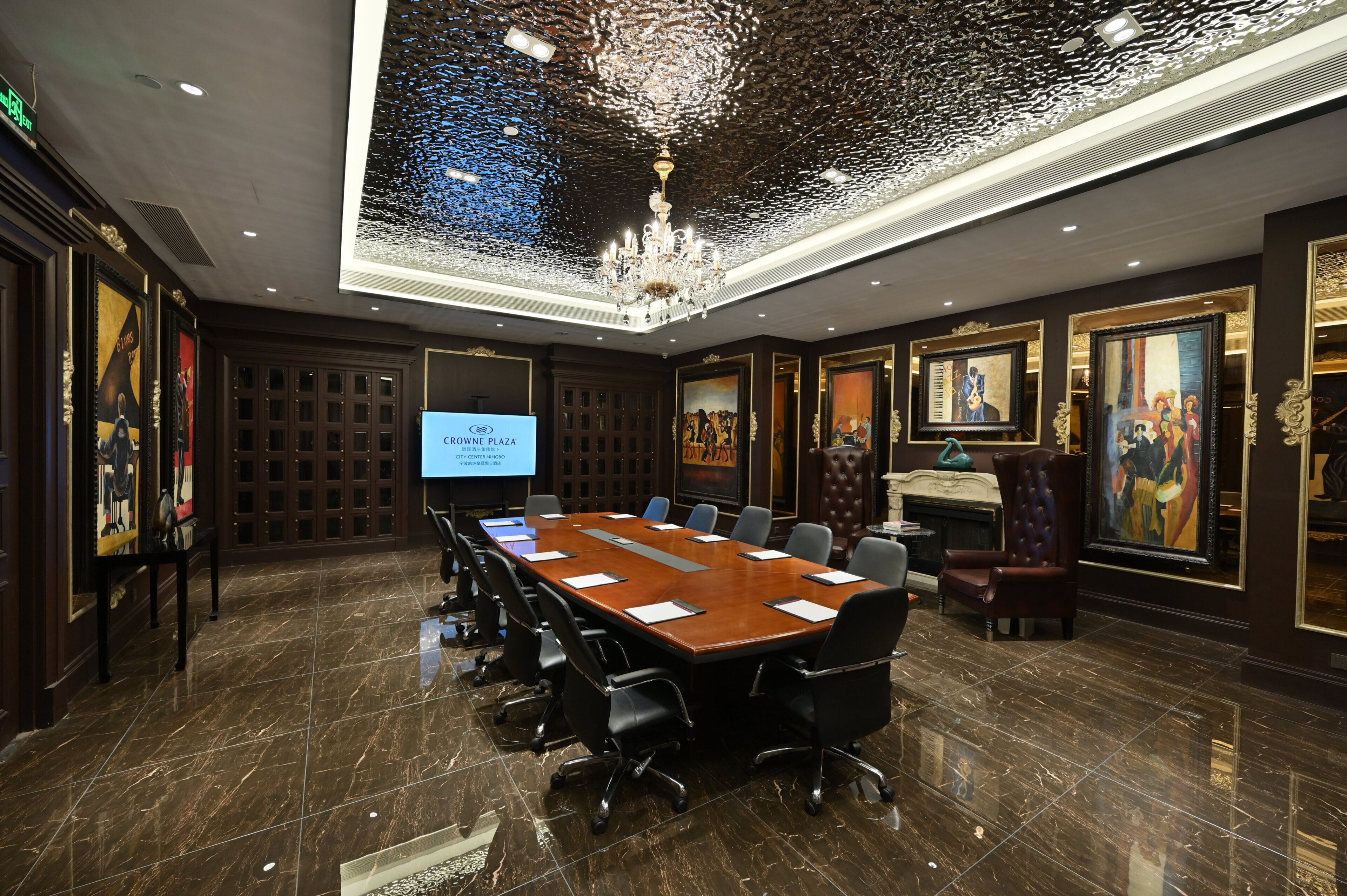 A conference room with a long table, chairs, a projector screen, and framed artwork on the walls.
