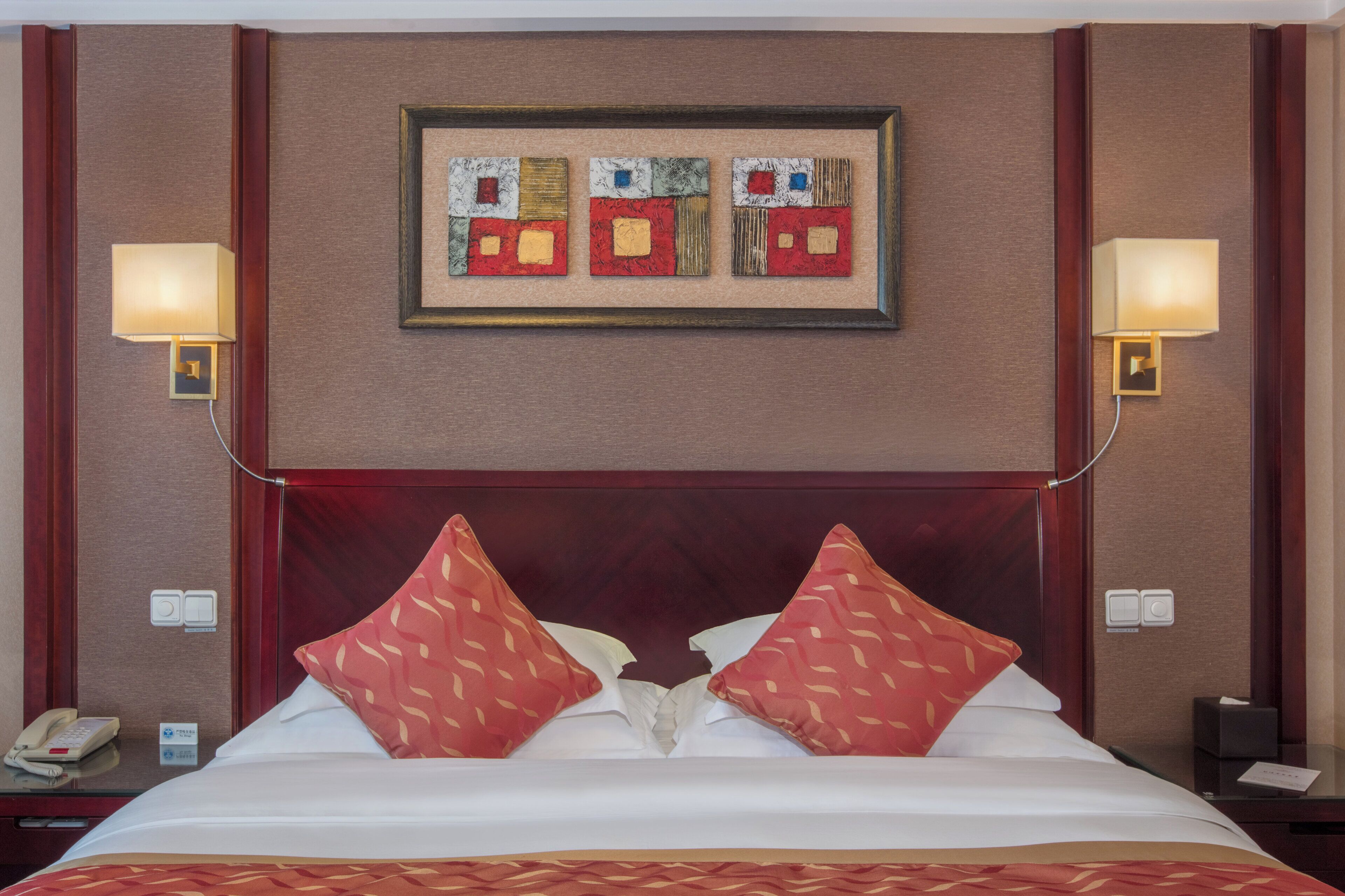 A hotel room with a large bed, two bedside lamps, a telephone, and a framed artwork above the bed.