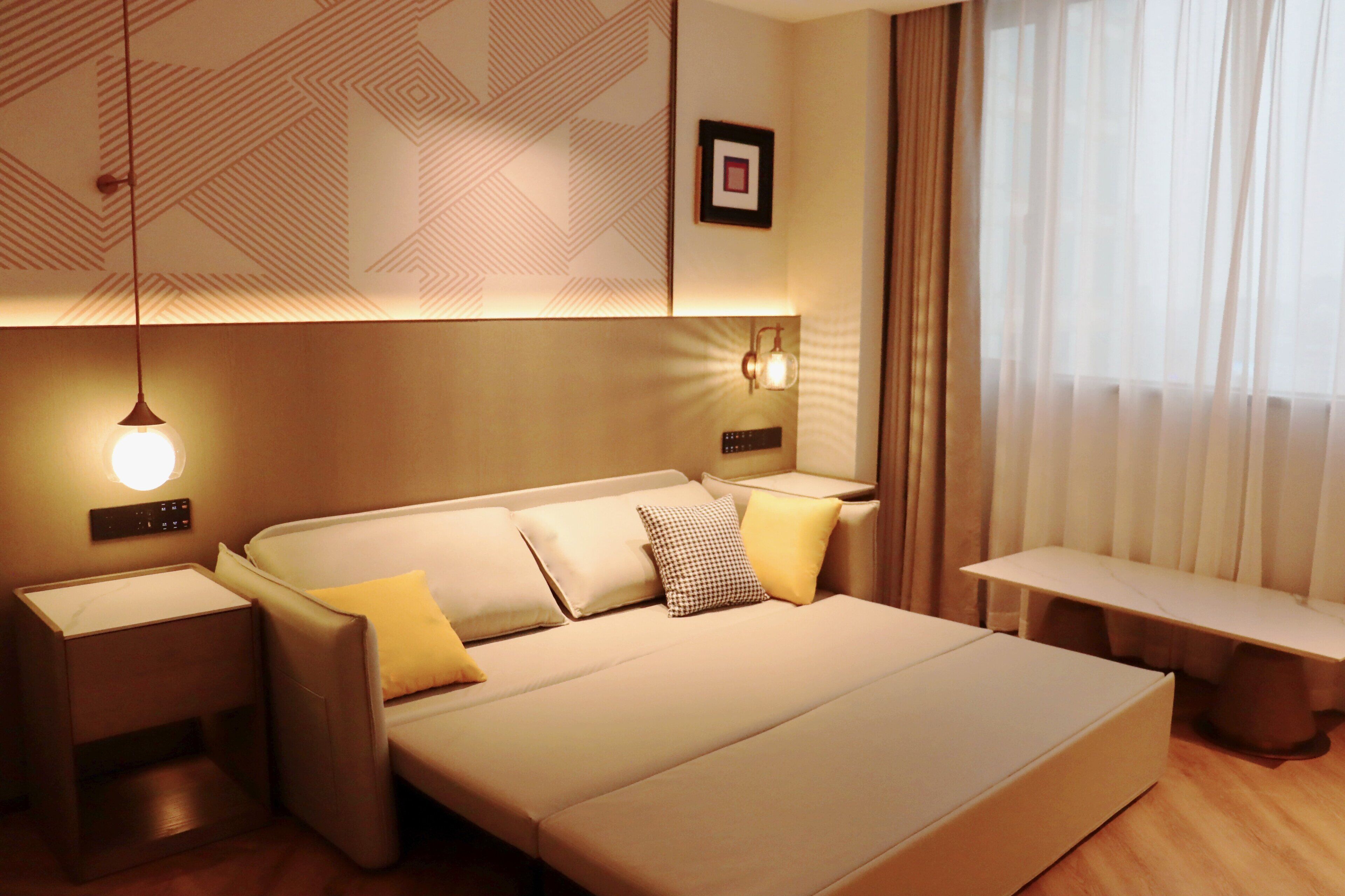 A modern bedroom with a large bed, bedside tables, a bench, and a wall-mounted light fixture.