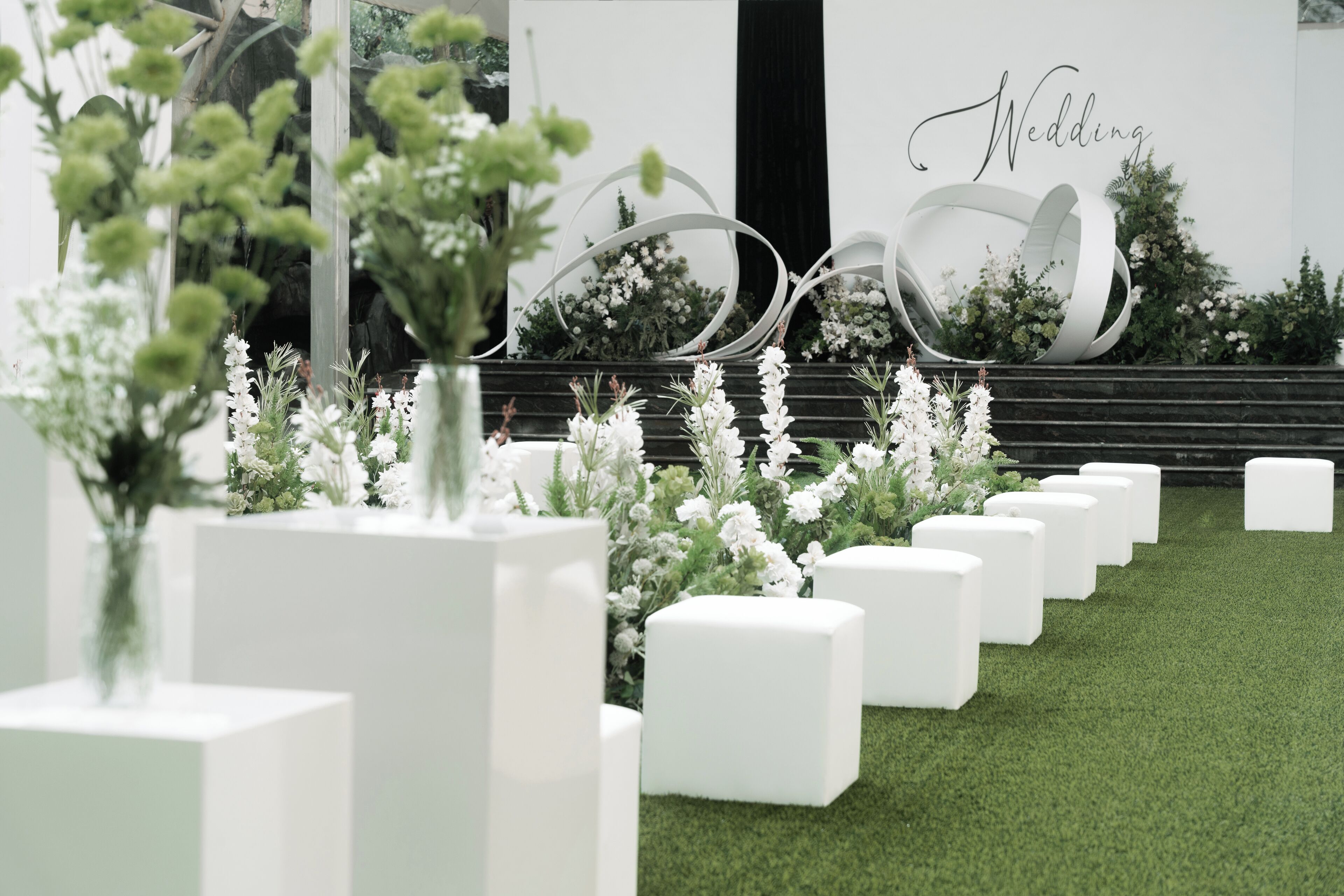 Un salón de bodas moderno con macetas blancas y césped artificial verde.