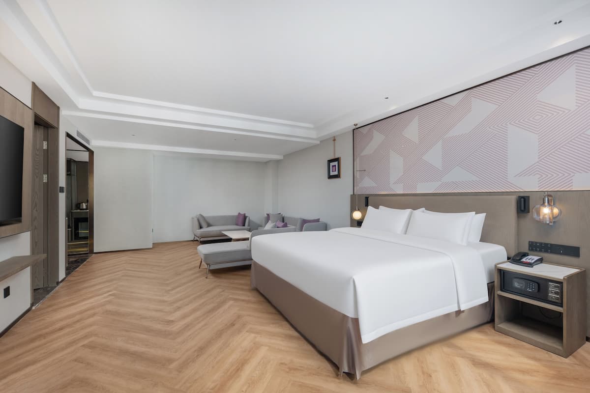 Una habitación de hotel moderna con una cama grande, un sofá, un televisor y una mesita de noche con un teléfono y una lámpara.