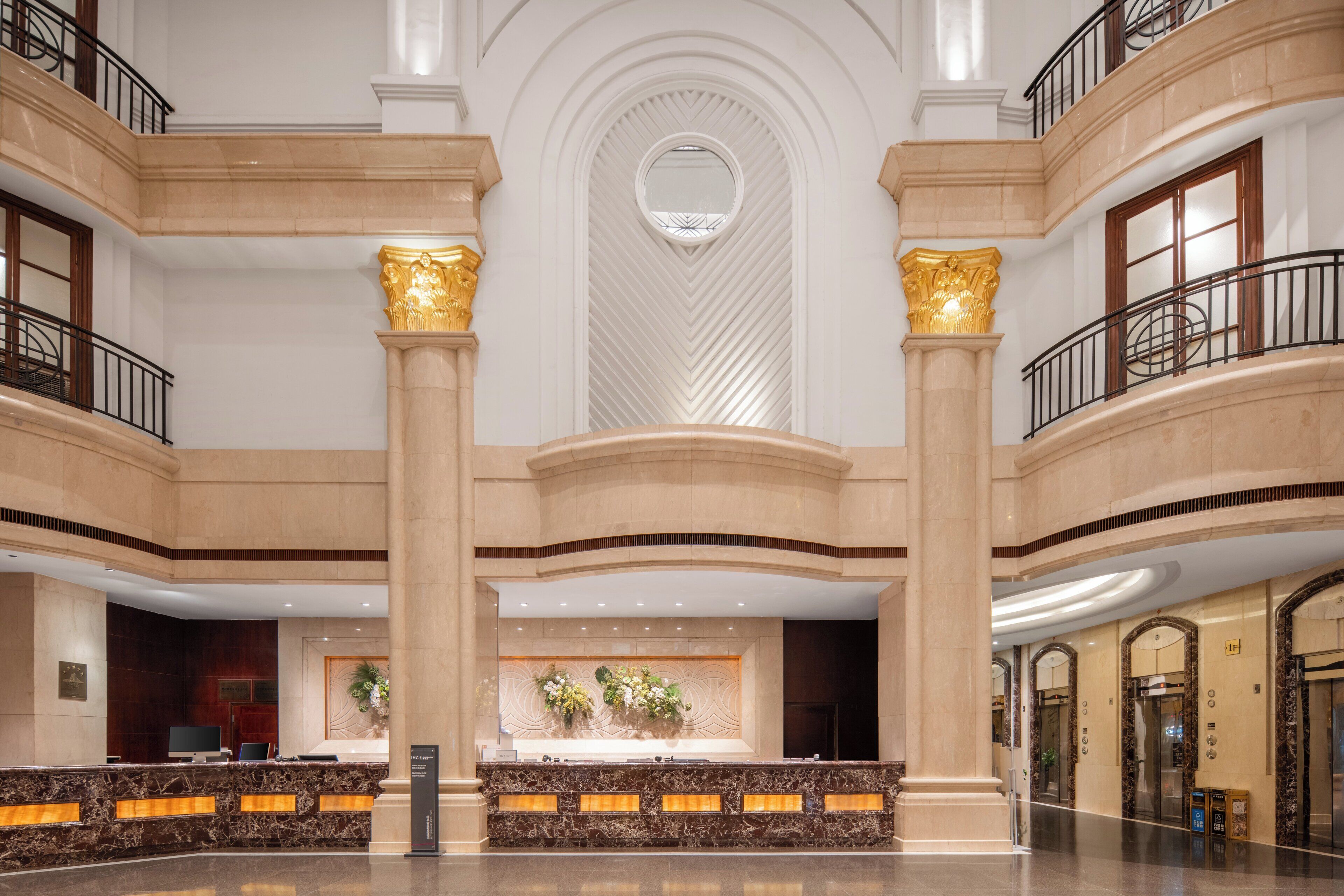 A spacious lobby with marble reception counters, a central decorative wall, and a modern elevator.
