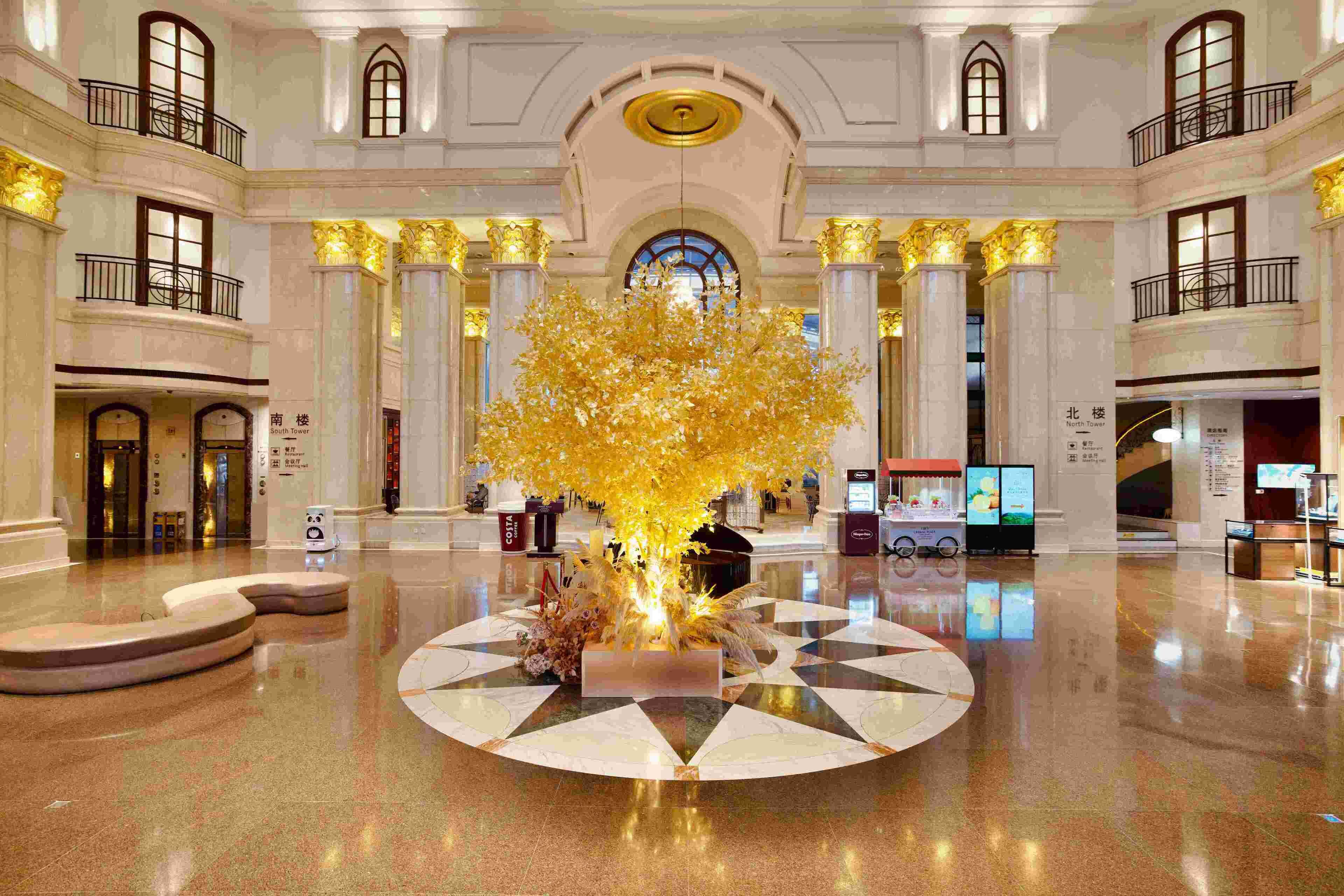 Een ruime lobby met een centrale decoratieve boom, verschillende verdiepingen en een gepolijste marmeren vloer.