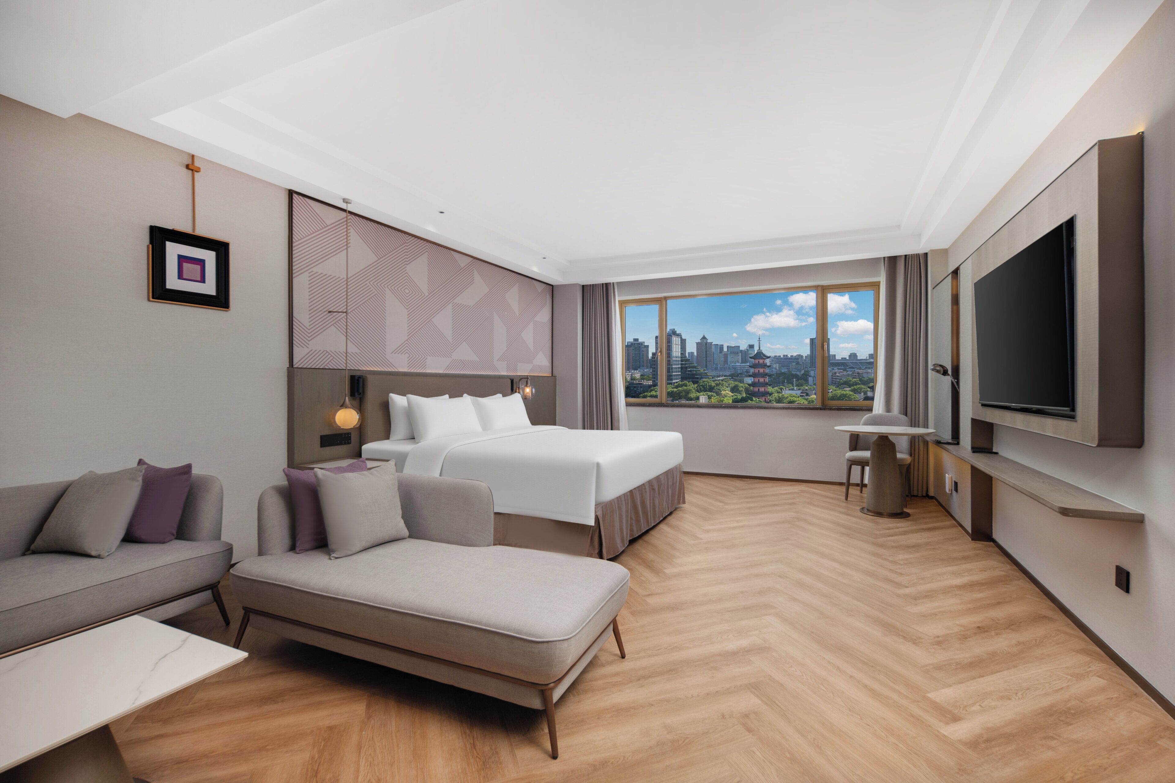 A modern hotel room with a city view, a sofa, a bed, and a TV.