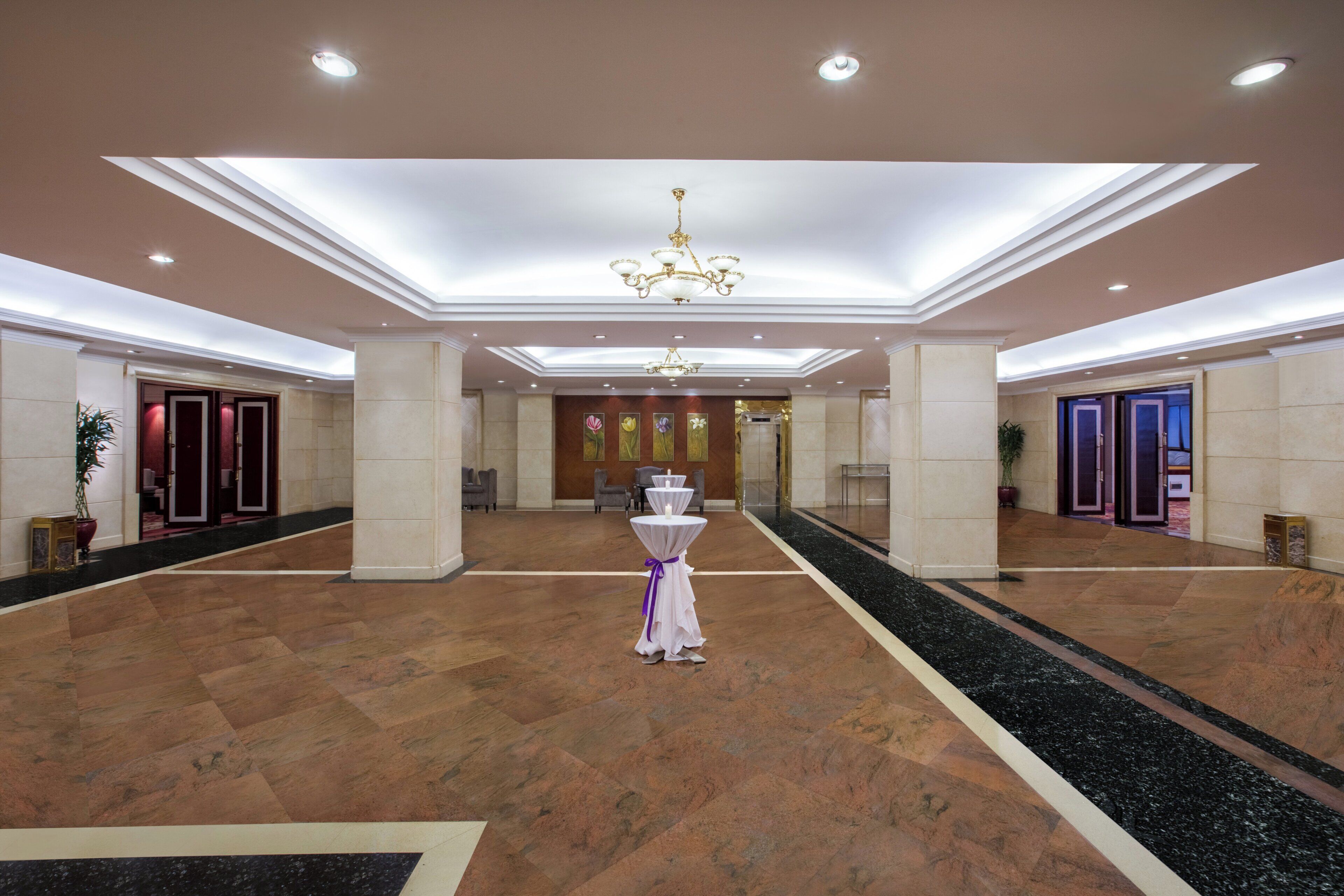 A spacious lobby with a central chandelier, marble flooring, and a reception desk.