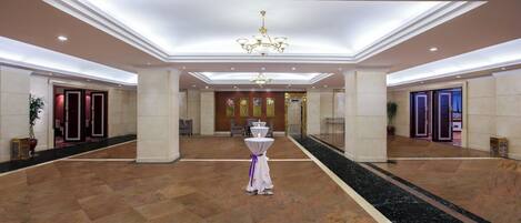 A spacious lobby with a central chandelier, marble flooring, and a reception desk.