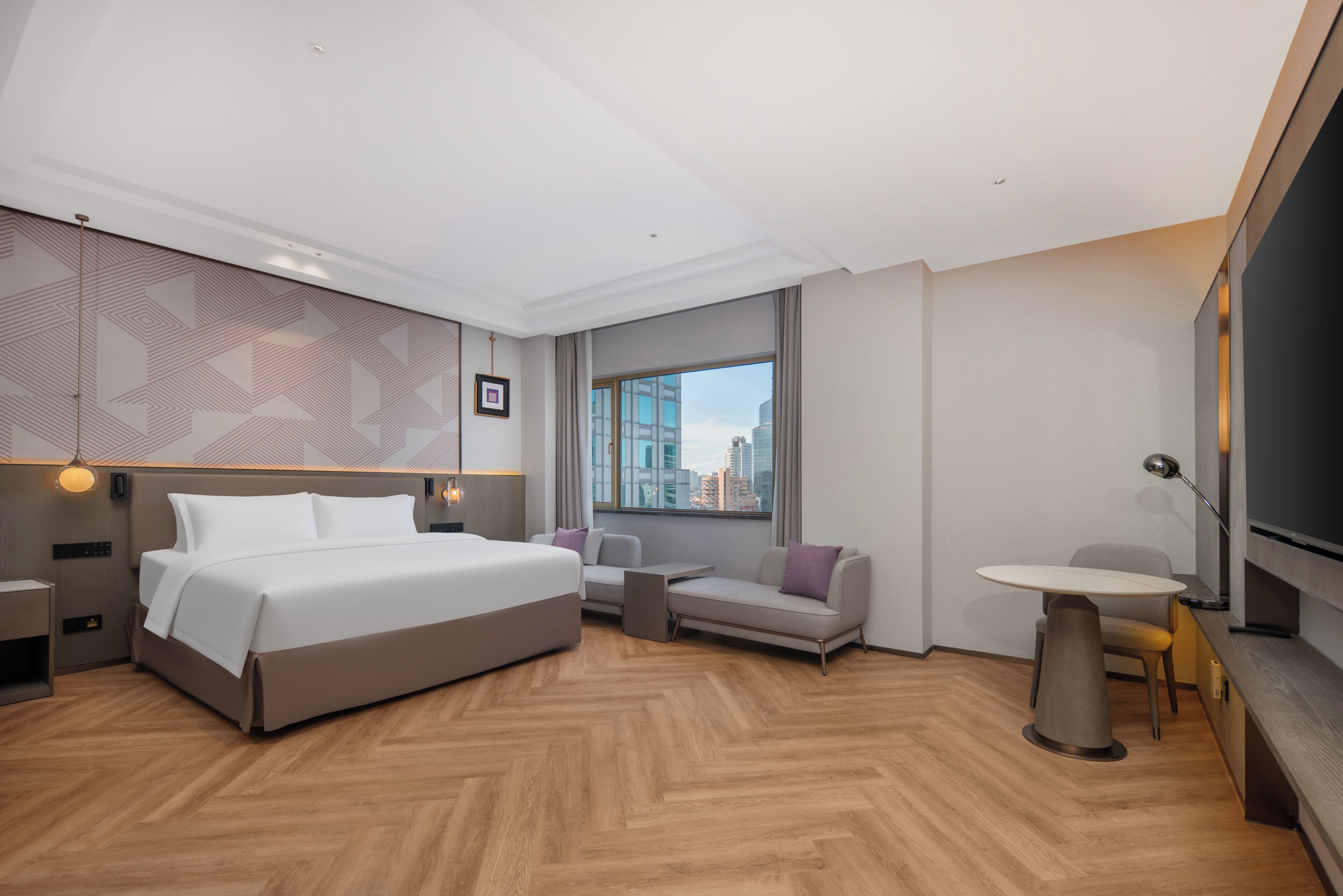 Una habitación de hotel moderna con una cama grande, un sofá, una mesita y un televisor.