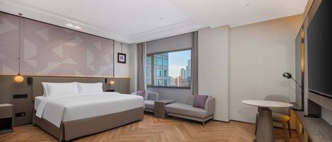Una habitación de hotel moderna con una cama grande, un sofá, una mesita y un televisor.