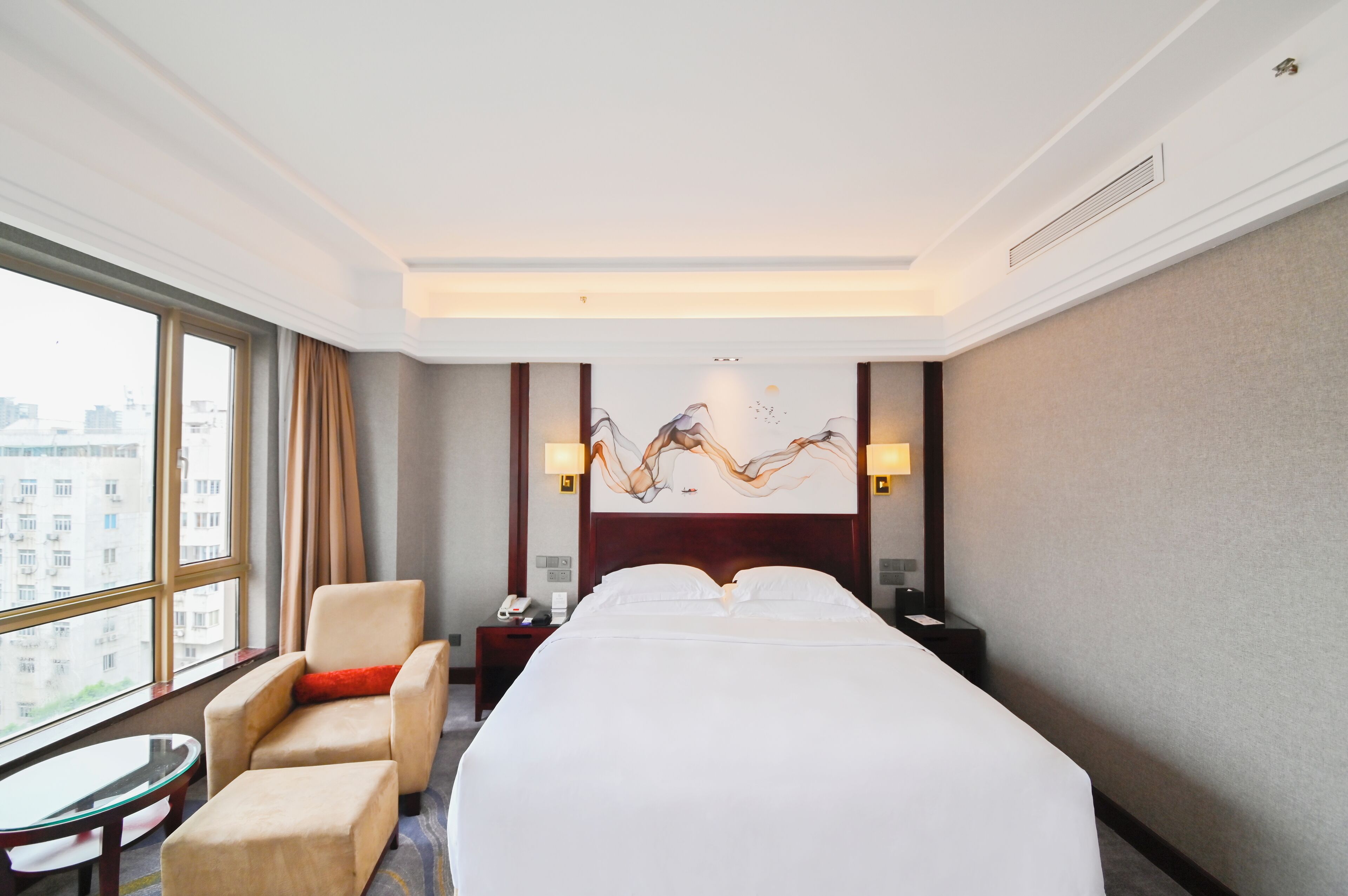 Una habitación de hotel con una cama grande, una silla, una mesita y un cuadro en la pared.