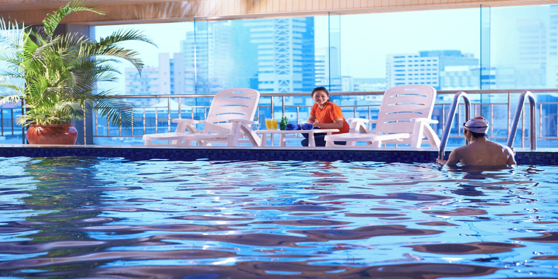 An indoor swimming pool with lounge chairs and a city view.