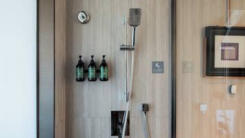 A shower area with a handheld showerhead, a wall-mounted faucet, and three bottles of body wash.