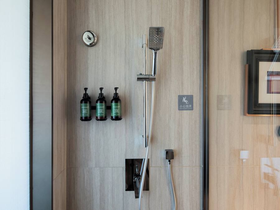A shower area with a handheld showerhead, a wall-mounted faucet, and three bottles of body wash.