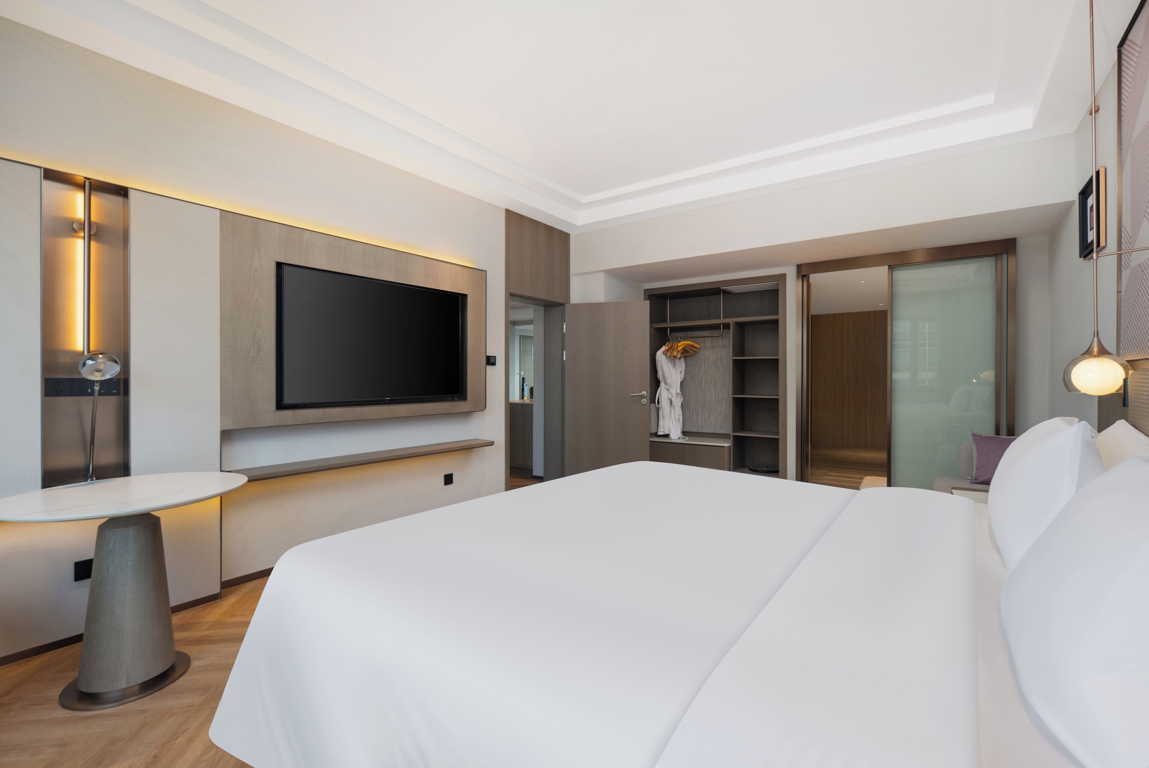 Una habitación de hotel moderna con una cama grande, un televisor de pantalla plana montado en la pared, una mesita redonda y un armario con puertas correderas.