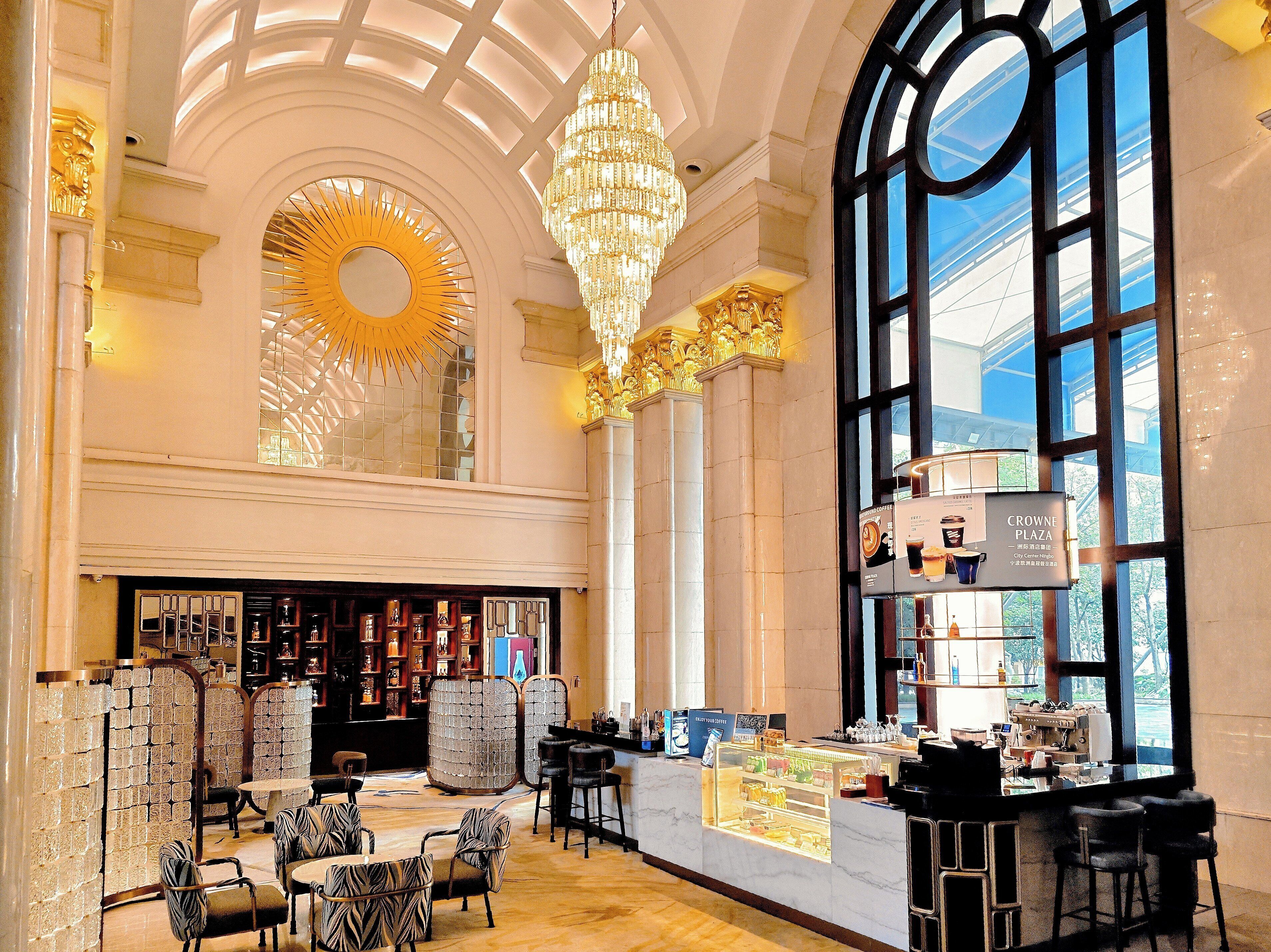 A spacious lobby with a grand chandelier, a coffee bar, and a large arched window.