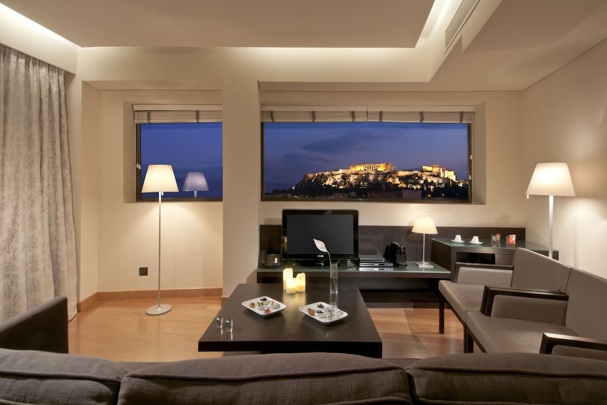 A modern hotel room with a large flat-screen TV displaying a cityscape, a cozy seating area with a coffee table, and a view of a historic building.