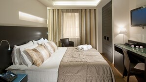 Habitación de hotel con cama, escritorio, silla, televisor y panel de control.