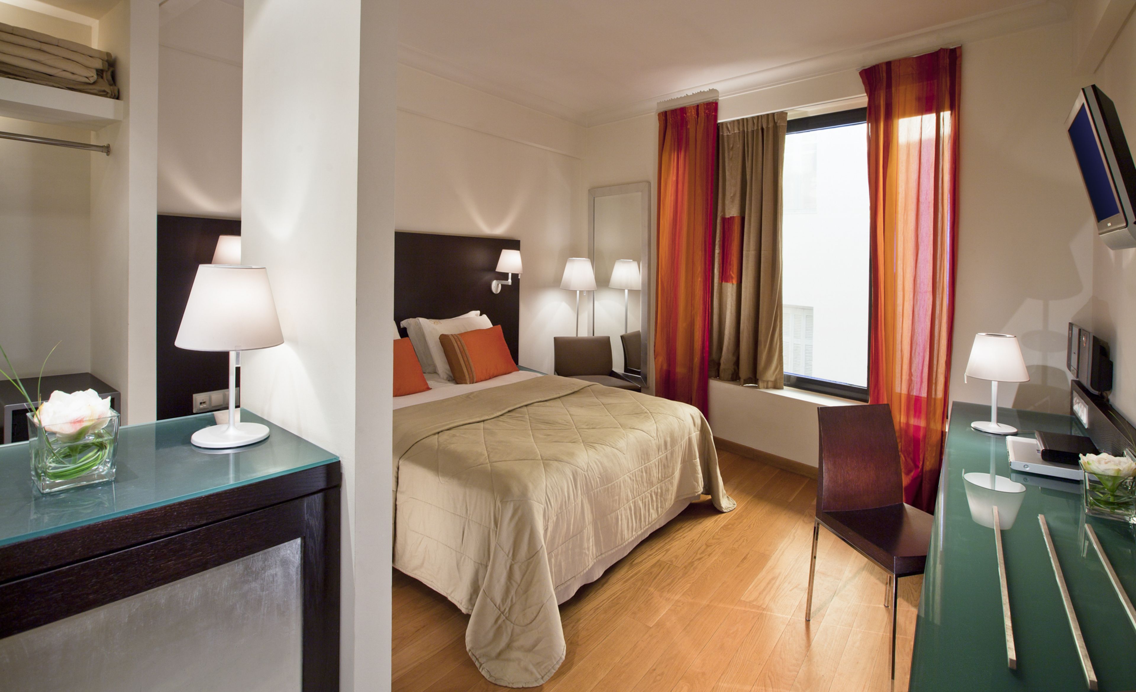 A hotel room with a bed, bedside lamps, a desk with a computer, and a window with curtains.