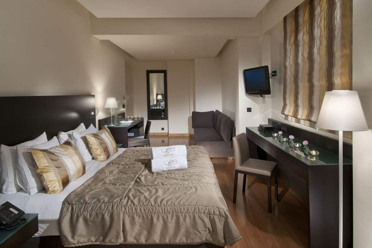 A hotel room with a large bed, a desk with a computer, a TV mounted on the wall, and a chair.